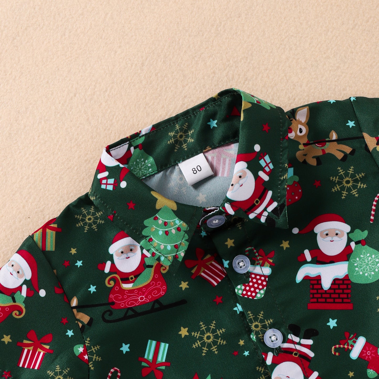 Close-up of a festive green shirt with colorful Christmas-themed prints, including Santa, reindeer, snowflakes, and presents. The size tag reads "80" on the collar.