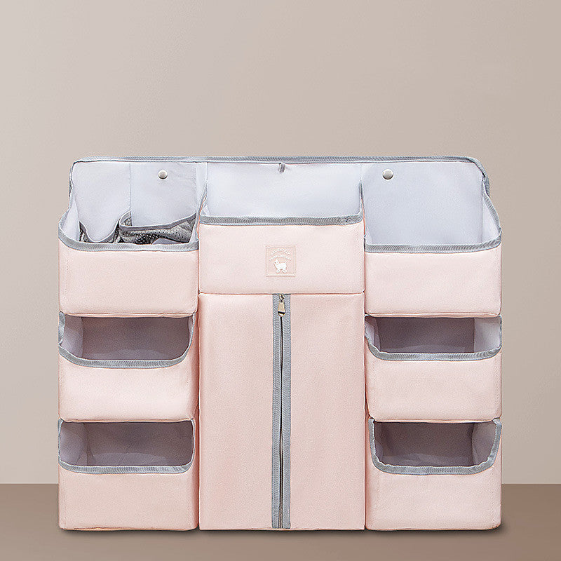 Pink hanging organizer for baby essentials with multiple compartments and a central zippered pocket. Designed for easy storage and accessibility.