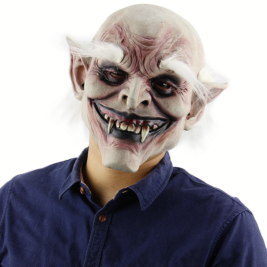 Person wearing a demonic mask with exaggerated features, including pointed ears, sharp fangs, and bushy white eyebrows, dressed in a blue collared shirt against a white background.