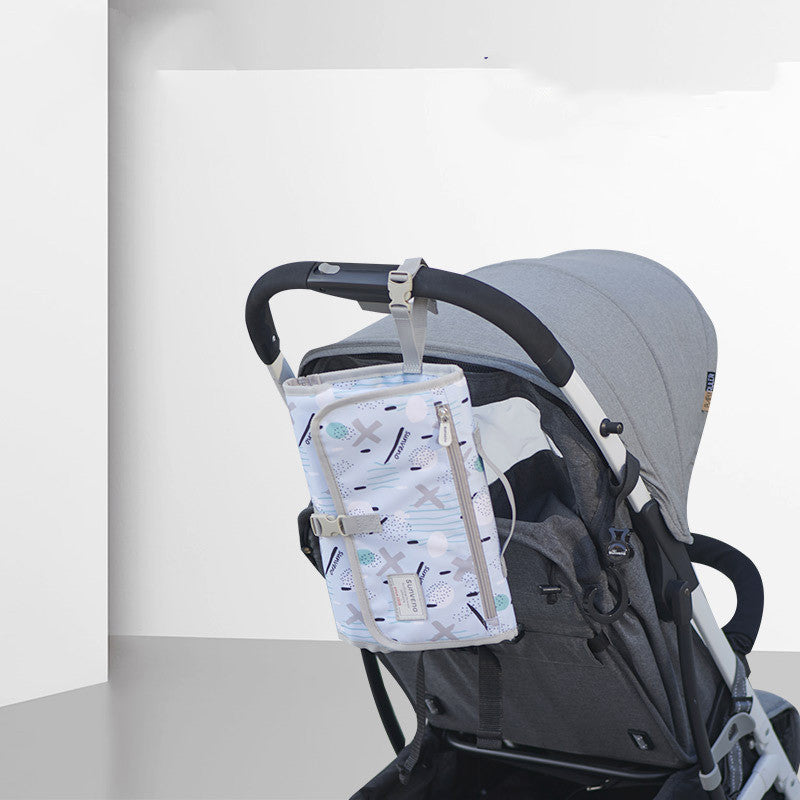 A gray stroller with a patterned blue and white bag attached to the handle, featuring a zipper and various designs. The stroller is positioned against a white and gray background.