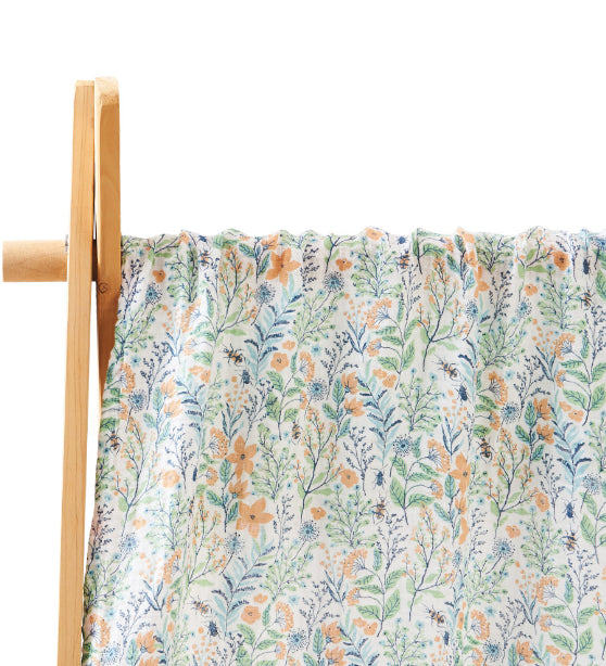 Floral patterned fabric with orange and blue flowers and green leaves, draped over a wooden frame. The background is white, highlighting the fabric's delicate design.