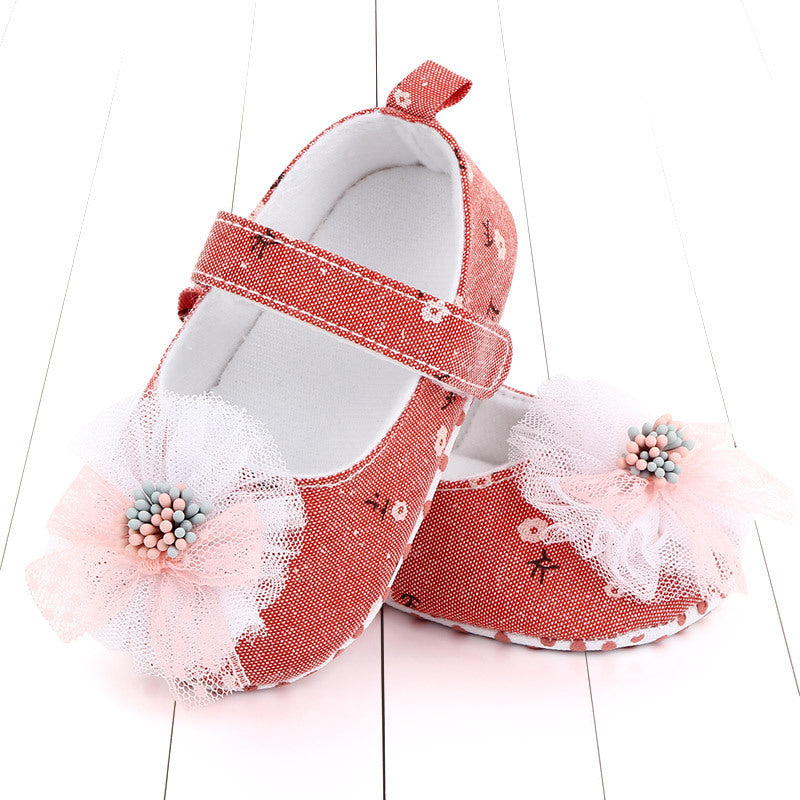 Red baby shoes with floral patterns, adorned with white lace flowers and pink and blue bead centers. The shoes have a Velcro strap and a loop at the heel for easy fastening.