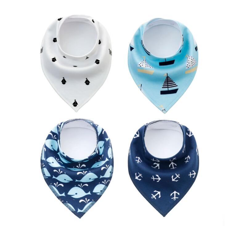 Four baby bibs in blue and white with nautical designs: ships on blue, anchors on navy, whales on dark blue, and boats on white. Bibs have a triangular bandana shape.