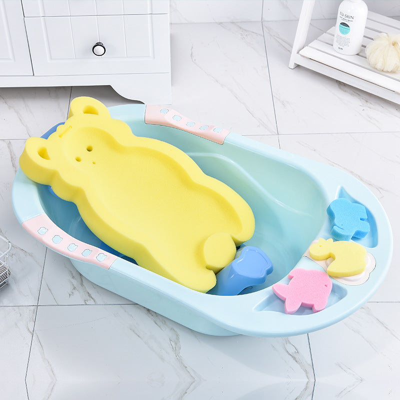 Baby bath setup with a blue plastic tub, yellow bear-shaped sponge, and colorful animal sponges. A bottle and luffa are on a nearby shelf in a tiled room.