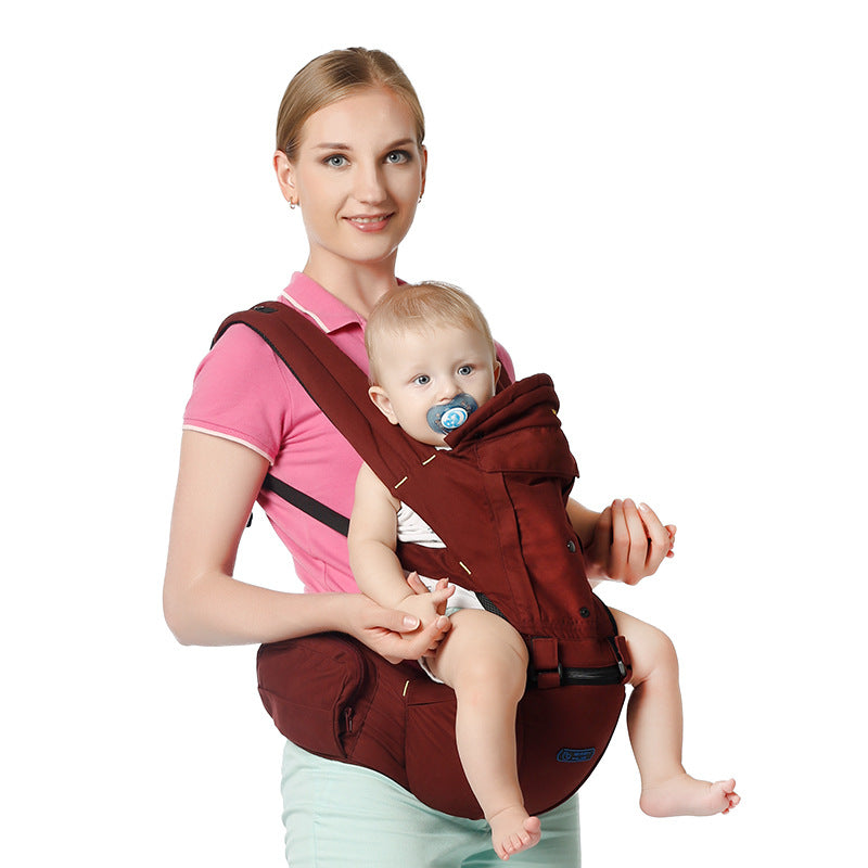 Smiling woman in a pink polo shirt holds a baby wearing a blue pacifier, seated in a maroon baby carrier. The background is white, highlighting the pair.