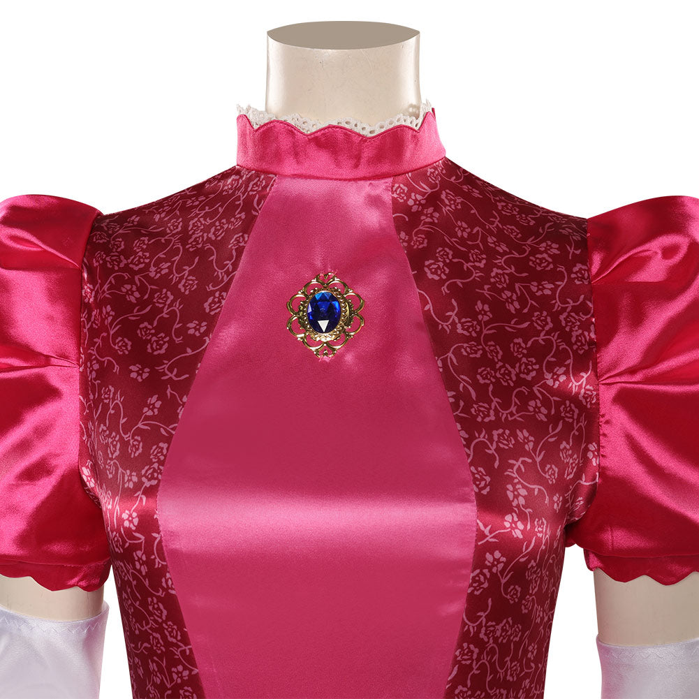 Close-up of a vibrant pink satin dress with intricate floral patterns and puffed sleeves. The collar is scalloped with lace trim, and a decorative blue gem brooch adorns the front.
