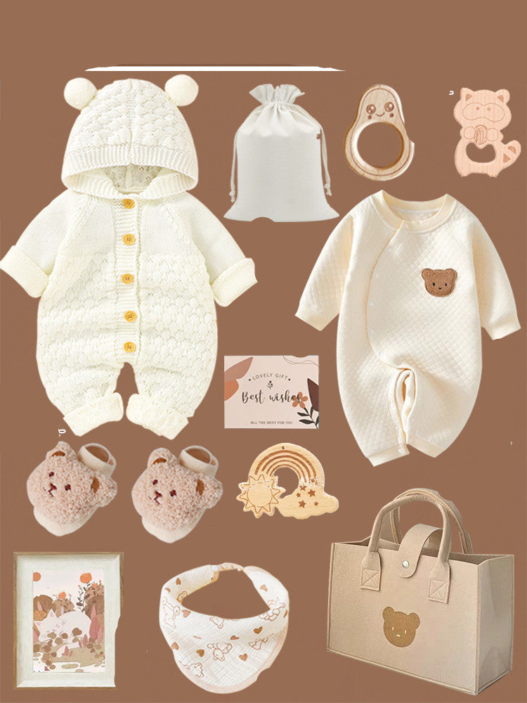 Assortment of baby items on a brown background, including a cream knitted onesie with bear ears, mittens, a bib, wooden toys, a gift bag, and a card.