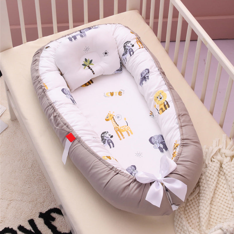Baby crib with an animal-print baby nest featuring giraffes, lions, and elephants on a white and gray cushion, tied with a white bow, inside a beige crib.