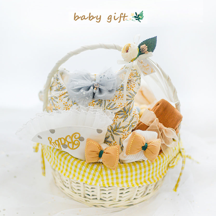 A woven basket adorned with a yellow gingham cloth, containing a floral-patterned pillow, bows, fabric flowers, and a frilly white bib with "Love" in gold lettering.