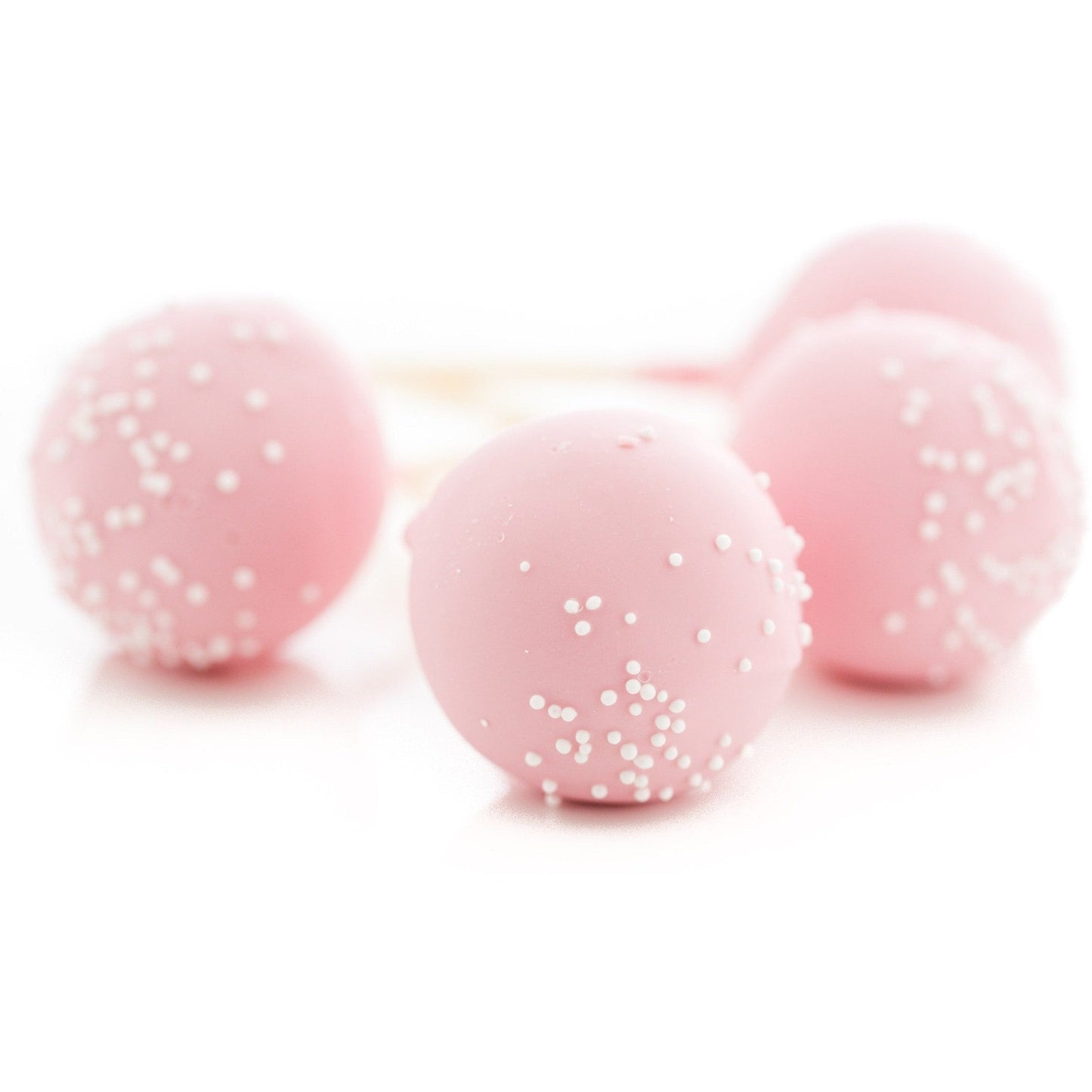 Close-up of four pink cake pops with white sprinkles, arranged on a white background. The cake pops are round, emphasizing their smooth texture and decorative sprinkles.