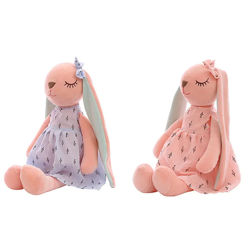 Two plush bunny toys wearing dresses; one in a blue dress with a blue bow, the other in a pink dress with a pink bow. Both have long ears and closed eyes.