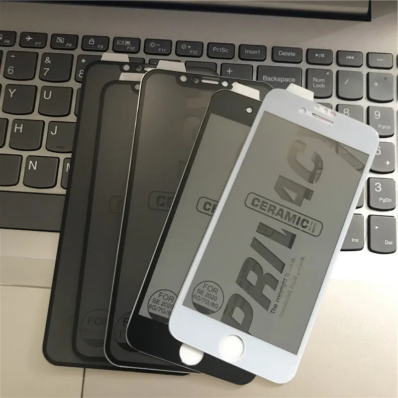 Four smartphone screen protectors, labeled "Ceramic Privacy," are fanned out on a laptop keyboard. They are designed for different iPhone models, with black and white frames.