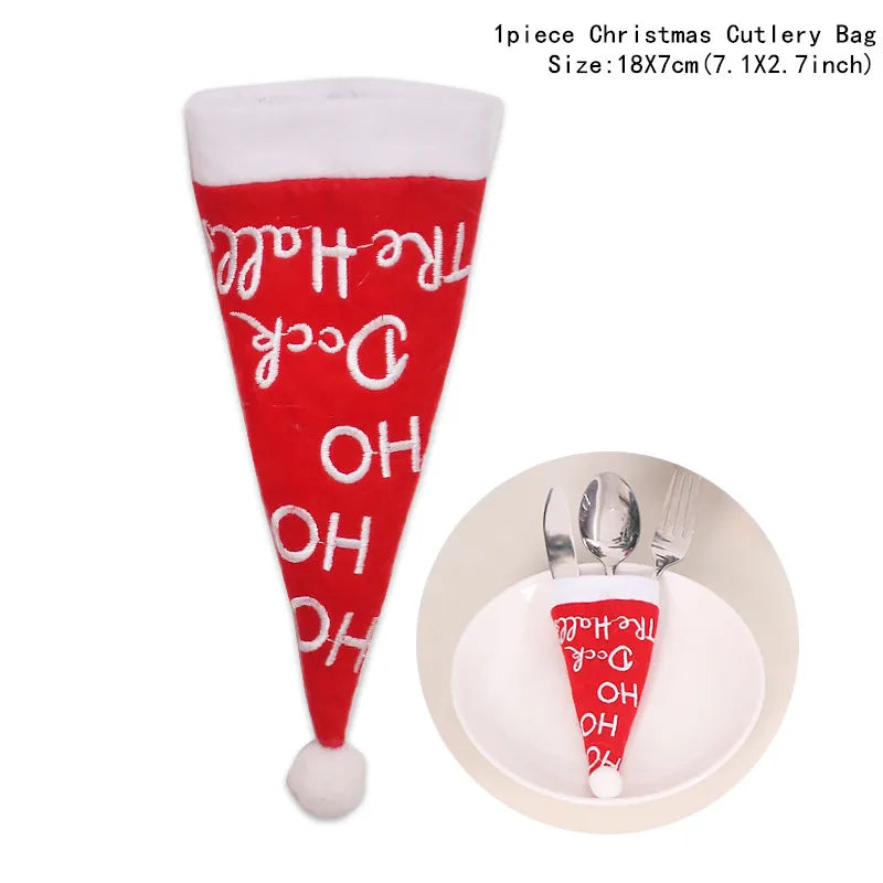 Red Christmas cutlery holder shaped like a Santa hat with white text and a pom-pom. The holder is displayed over a white plate with a fork and a spoon.