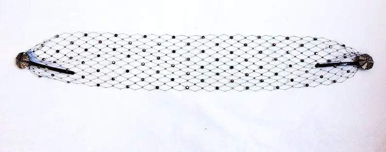 A decorative black mesh hair net with diamond patterns, adorned with small black dots. It features ornate circular clips on each end, embellished with rhinestones and black accents.