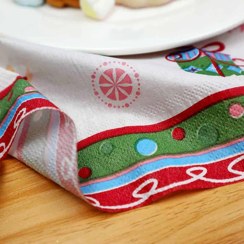 Festive paper napkin with colorful designs, including a wrapped gift and candy patterns, folded beside a white plate on a wooden table.