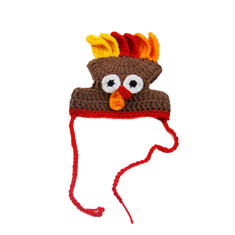Crocheted turkey hat featuring brown body, colorful feathers, googly eyes, an orange beak, and red ties; resembling a festive bird for seasonal wear.