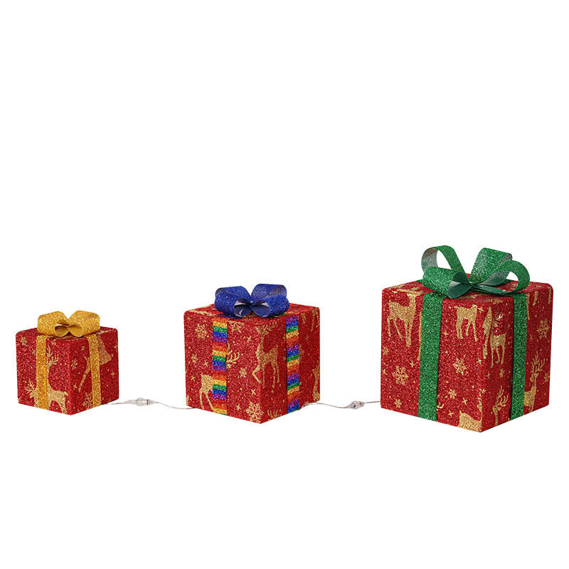 Three glittery red gift boxes, each with a different colored bow—yellow, blue, green—and reindeer patterns. The boxes are connected by a string of lights.