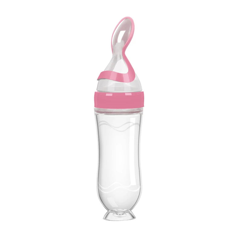 Transparent squeeze bottle with pink accents, features an integrated spoon. Designed for feeding babies, the bottle is upright with a rounded base and wavy sides.