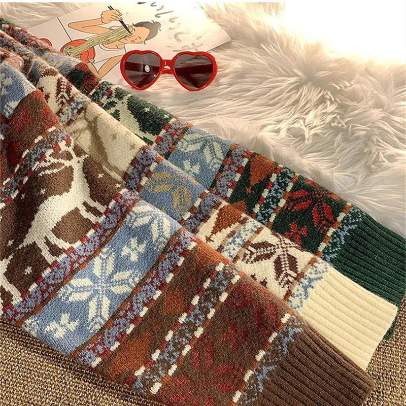 Knitted sweaters with festive deer and snowflake patterns in earthy colors are layered on fluffy fabric, accompanied by red heart-shaped sunglasses and a cartoon magazine.