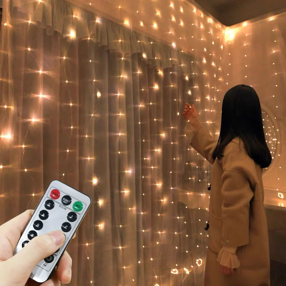 A person wearing a long coat stands near a curtain adorned with warm, glowing string lights. A hand holding a remote control is visible in the foreground, adjusting the lights.