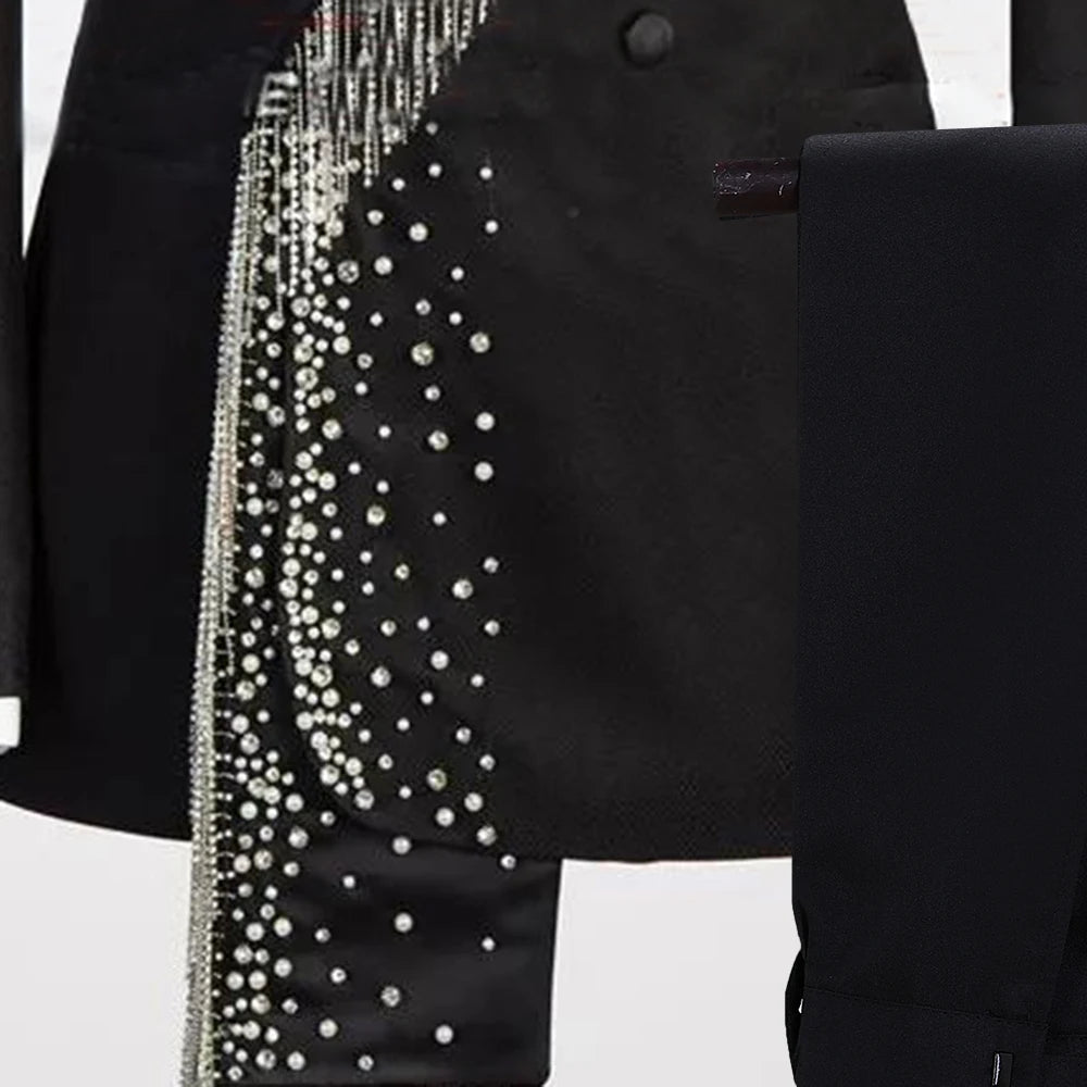 A black suit jacket adorned with shimmering silver chains and pearl-like embellishments cascading diagonally. A white shirt and black tie are visible beneath.