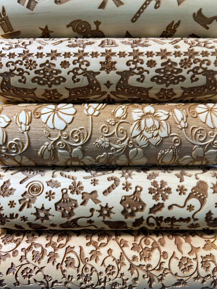 Close-up of five wooden rolling pins with intricate engraved designs featuring festive motifs like reindeer, snowflakes, flowers, and Christmas ornaments in a warm, natural tone.