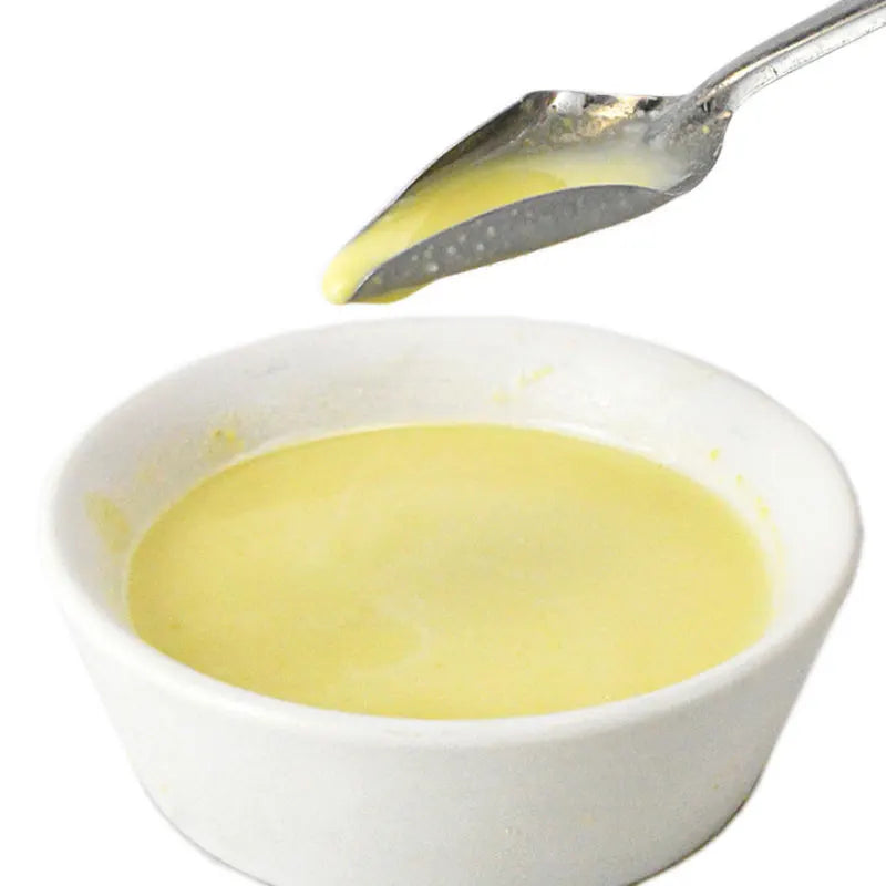 A spoon drips creamy yellow custard into a small white bowl filled with the same custard.