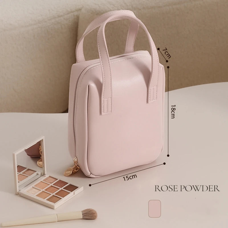 A small, pink makeup bag labeled "Rose Powder" on a table with a makeup palette and brush. The bag's dimensions are 15cm x 18cm x 7cm.