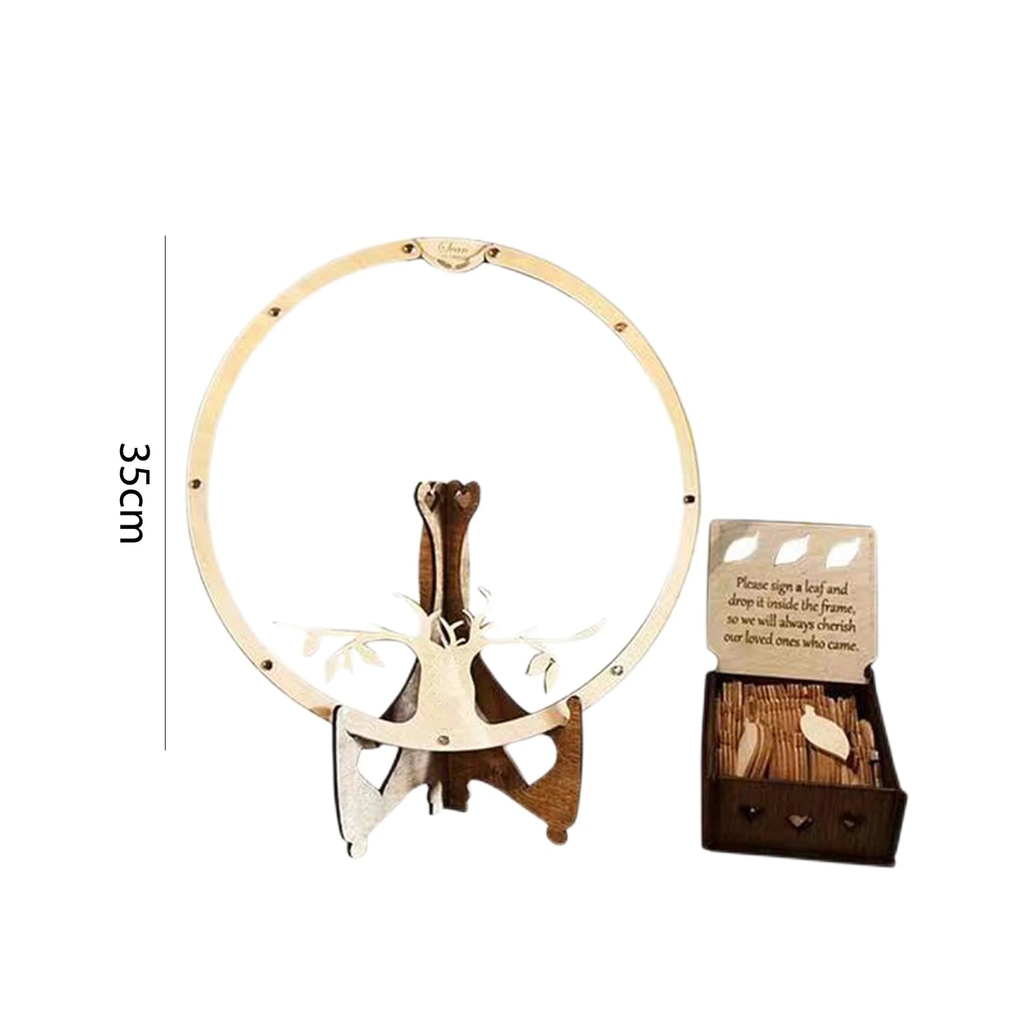 Wooden circular frame on a stand, 35cm tall, with a box of wooden leaves. A sign invites guests to sign and insert leaves into the frame for remembrance.