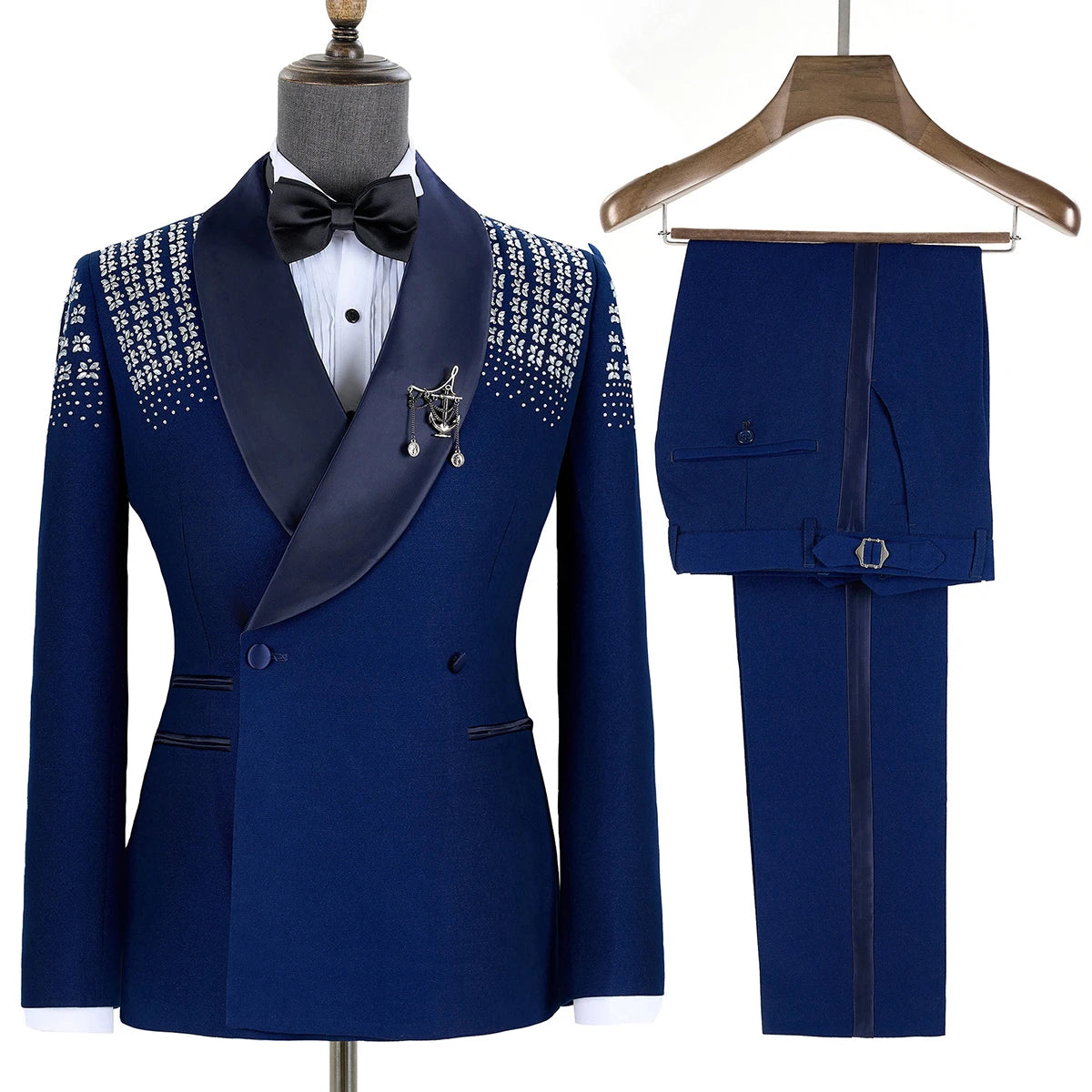 Elegant royal blue tuxedo with a satin shawl lapel, embellished with intricate white patterns on shoulders, displayed with matching trousers on a wooden hanger.