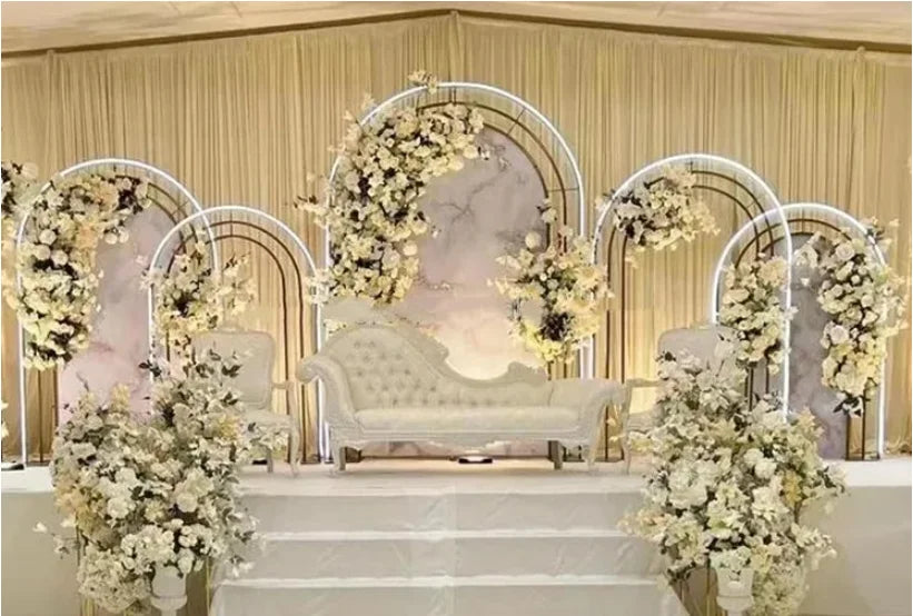 Elegant wedding stage with a white tufted loveseat, surrounded by floral arches and arrangements in cream and white tones. Draped backdrop adds a sophisticated touch.
