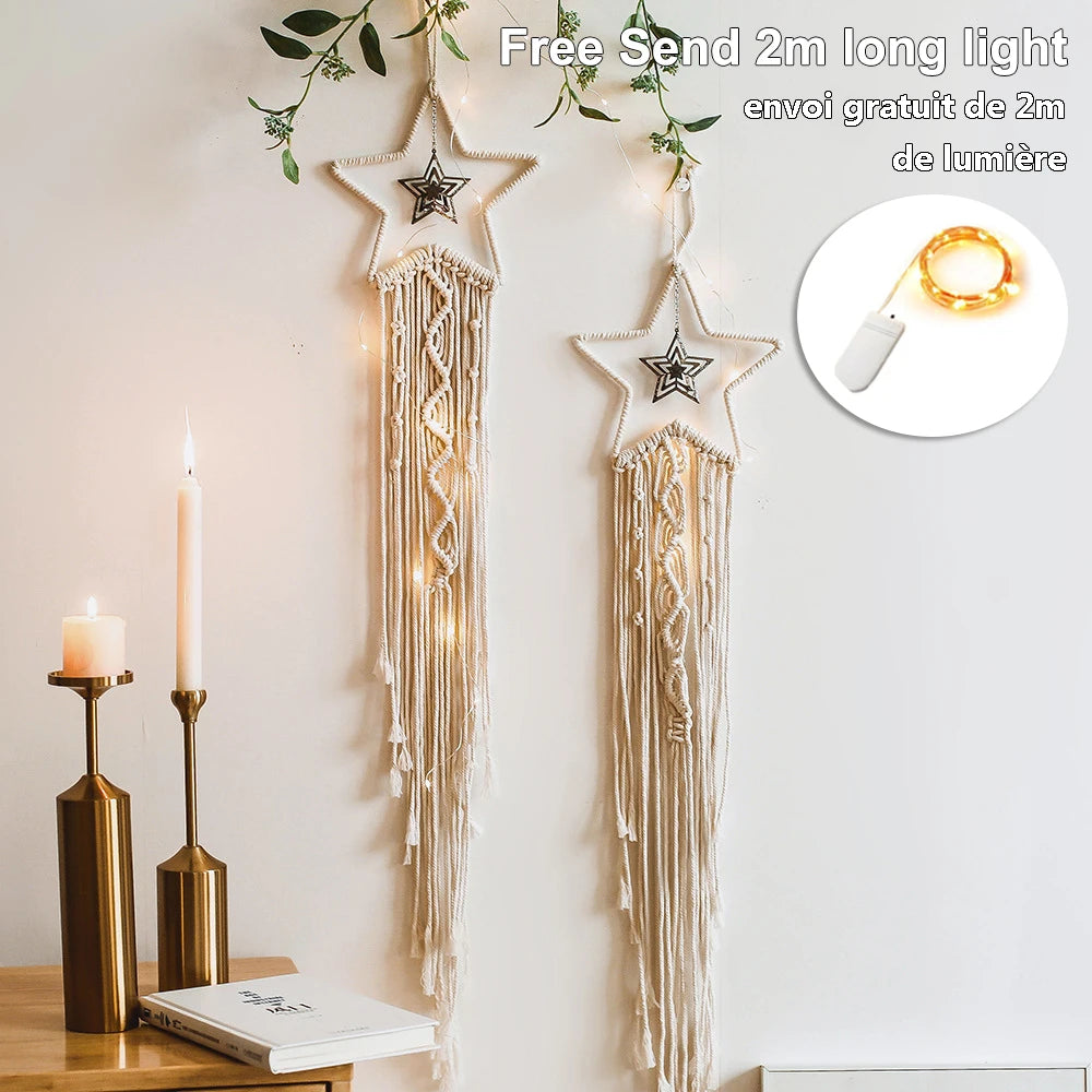 Macramé wall hangings shaped like stars with string lights and leaves. Nearby, two lit candles on gold holders rest on a table beside a closed book. Includes a 2m light offer.