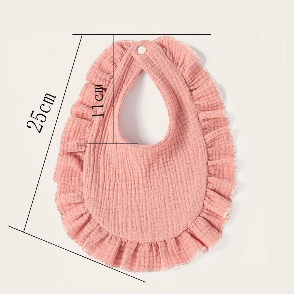 Pink ruffled baby bib with snap closure, measuring 25cm in length and 11cm at the neck. The fabric has a textured, crinkled appearance, giving it a soft, cozy look.