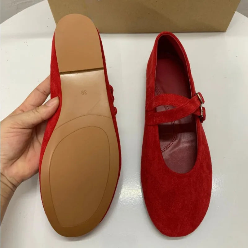 Red suede Mary Jane shoes with a flat sole and a double strap. One shoe shows the sole with size indicated, and the other is upright. Background shows a beige box.