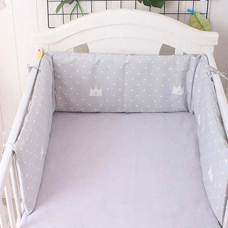 Gray crib with soft polka-dotted bumper pads adorned with crown graphics. The crib is made of white wood and has a pale purple mattress, creating a cozy environment.