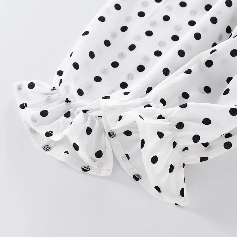 Close-up of a white fabric with black polka dots, featuring a frilled edge. The material has a soft, flowy texture and the pattern is uniformly distributed across the fabric.