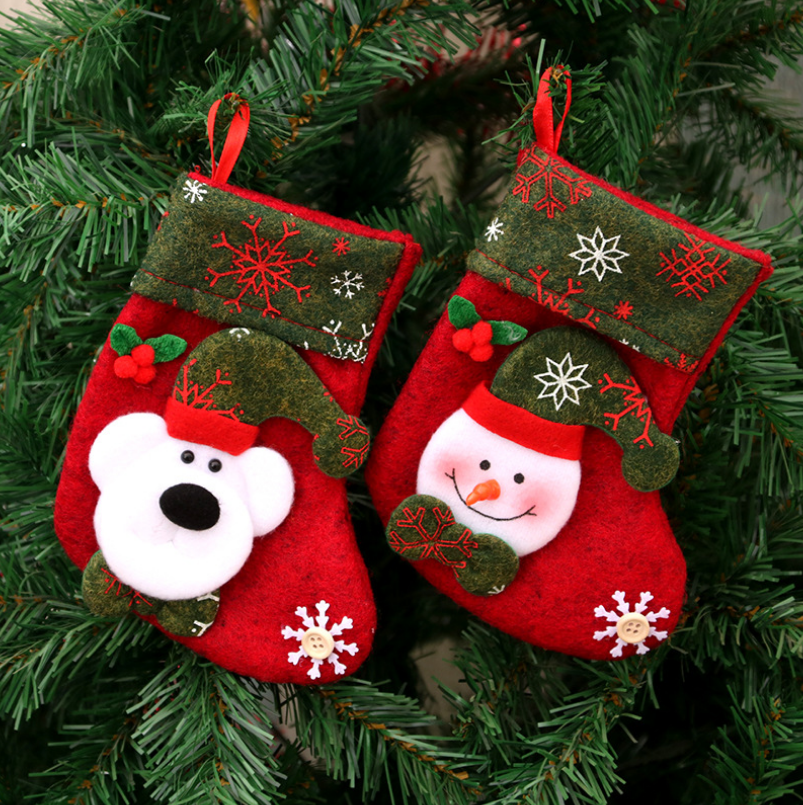 Two festive felt stockings hang on a Christmas tree. One features a snowman with a carrot nose, the other a polar bear. Both have green cuffs adorned with red snowflakes.
