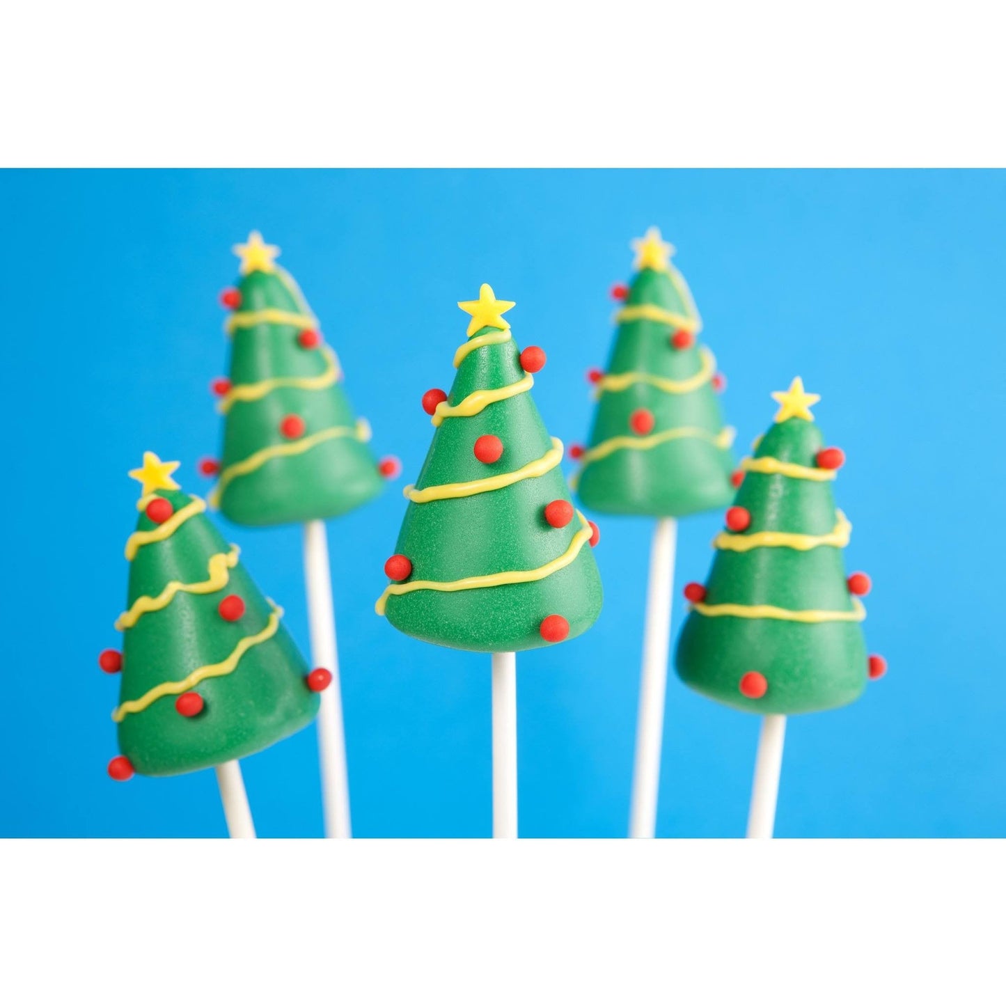 Five Christmas tree cake pops against a blue background, decorated with yellow icing garlands, red dots as ornaments, and topped with yellow stars.