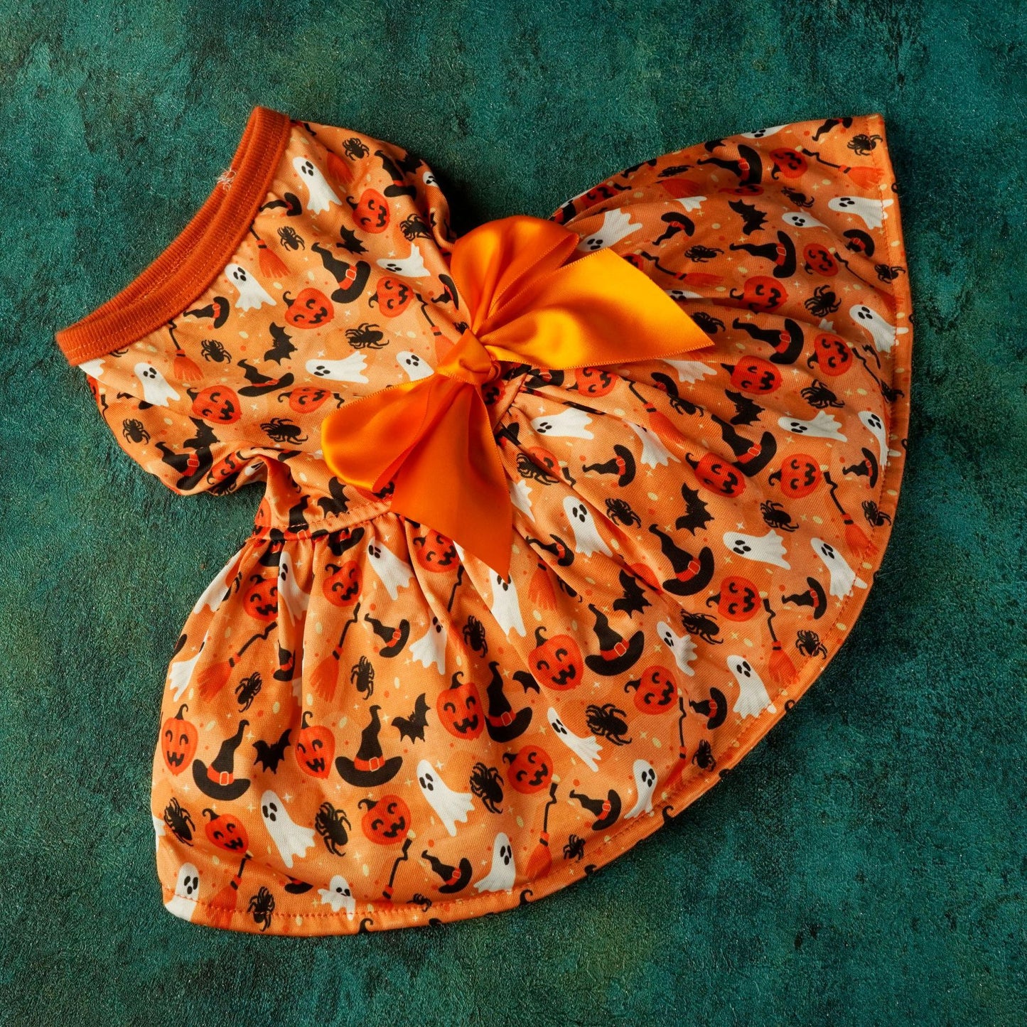 Orange Halloween-themed dress with a big satin bow, featuring ghost, pumpkin, spider, bat, witch's hat, and black cat patterns on a blue-green textured background.