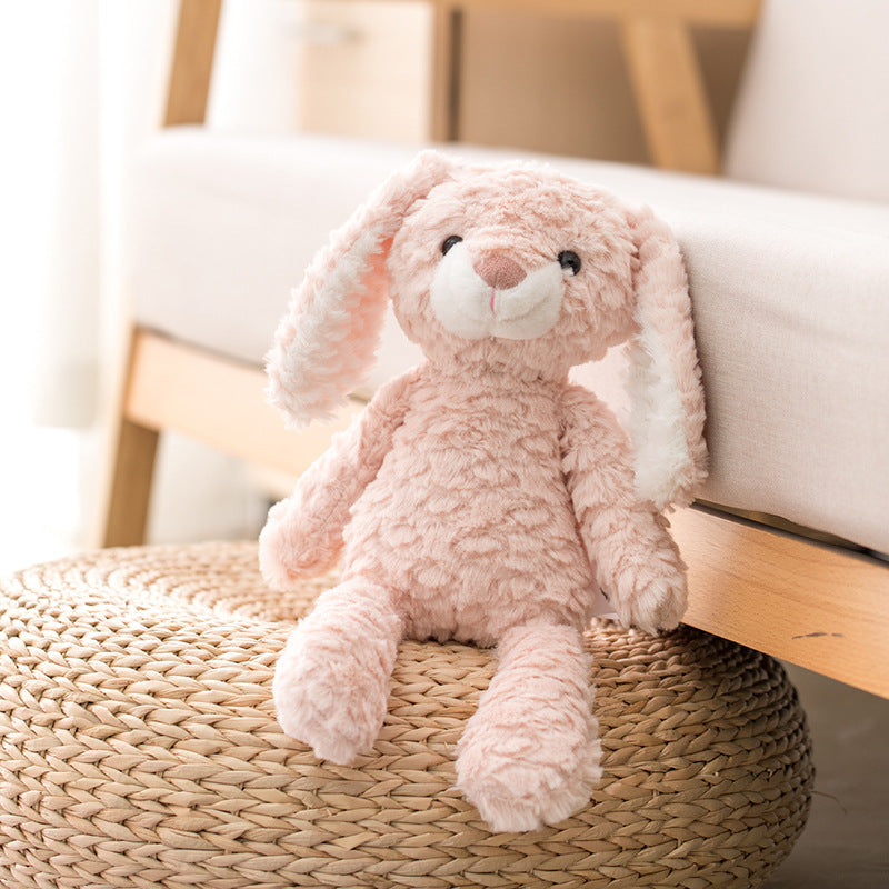 A plush pink bunny with long ears sits on a woven round stool next to a light-colored sofa in a cozy room.