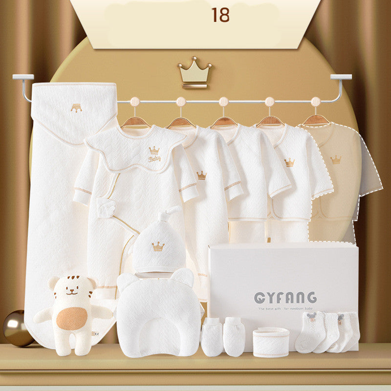 Baby clothing set displayed on hangers, featuring white outfits with crown motifs. Includes a soft toy, pillow, booties, and socks, all neatly arranged. Elegant and cozy presentation.
