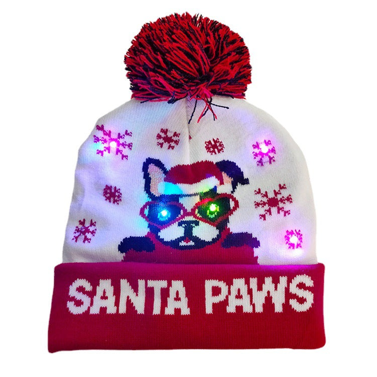 White beanie with red pom-pom, features a dog in Santa attire with LED lights. Surrounded by red snowflakes and "Santa Paws" text on red cuff.
