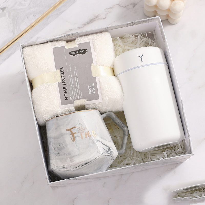 Gift box with a super soft white face towel, a white insulated bottle, and a marbled mug with "Fine" written on it. Items are arranged neatly on shredded paper.