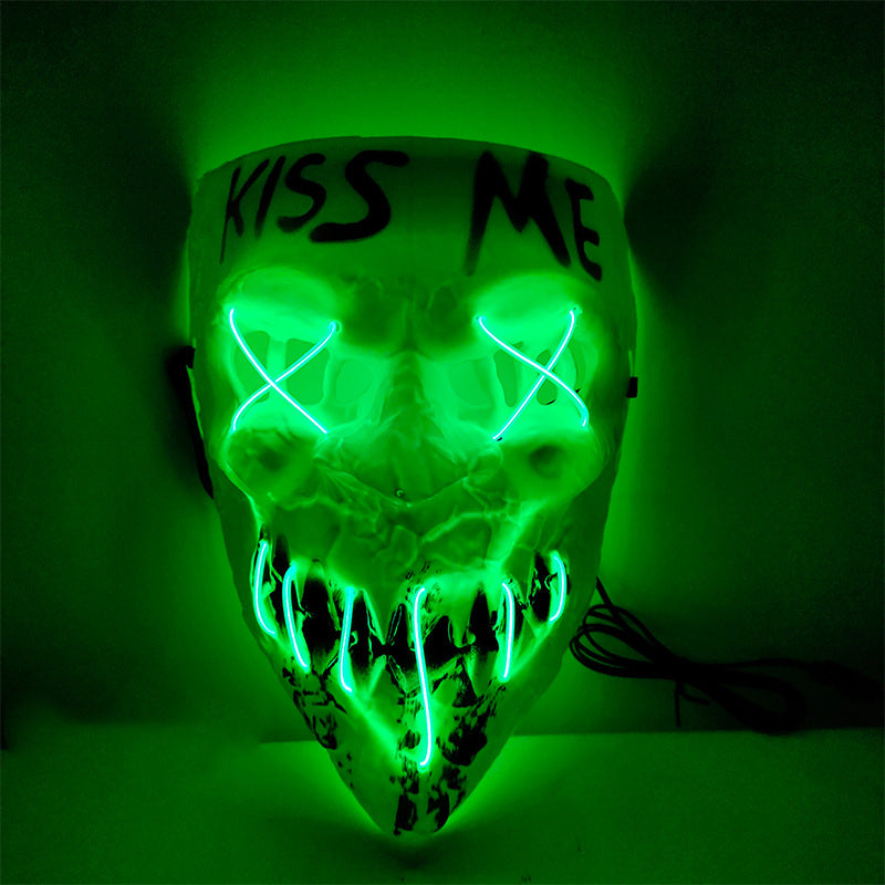 A glowing green mask with "Kiss Me" written on the forehead. It features stitched X eyes and sharp teeth outlined by neon lights, creating an eerie effect.