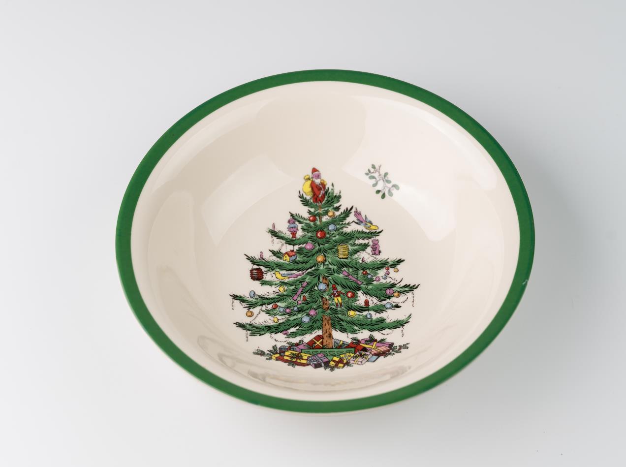 Ceramic bowl with a green rim, featuring a decorated Christmas tree design with presents at its base, set against a white background.
