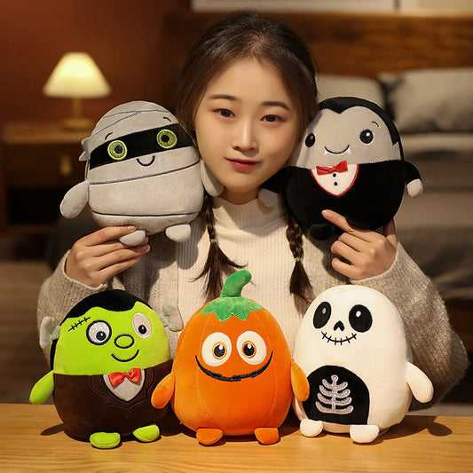 A person with braided hair holds five plush toys: a mummy, a vampire, a green Frankenstein's monster, a smiling pumpkin, and a skeleton. A warm lamp glows in the background.