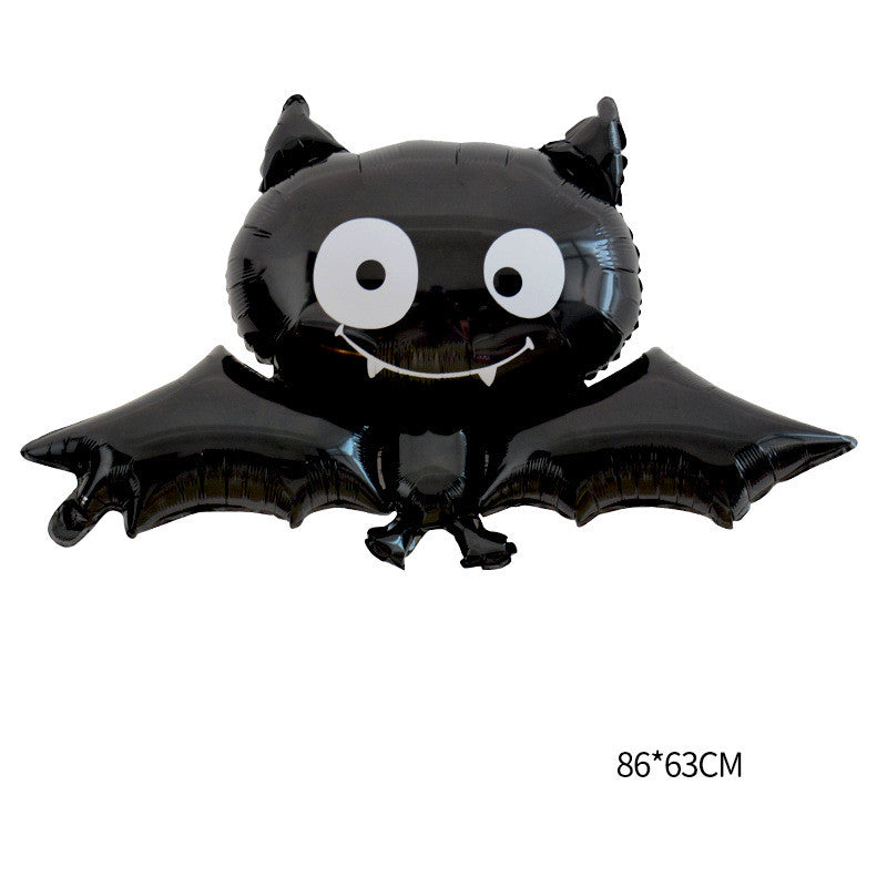 A shiny black bat-shaped foil balloon with large white eyes and small fangs. The wings are spread wide, giving it a playful appearance. The dimensions of the balloon are shown as 86 by 63 centimeters.