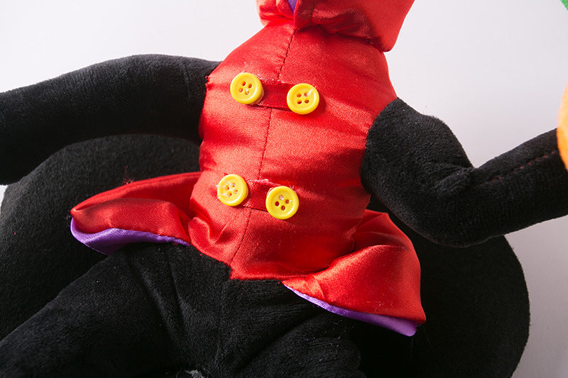 Close-up of a plush toy with a red satin top, yellow buttons, and black limbs. The outfit has a purple and red trim, and the background is a plain white surface.