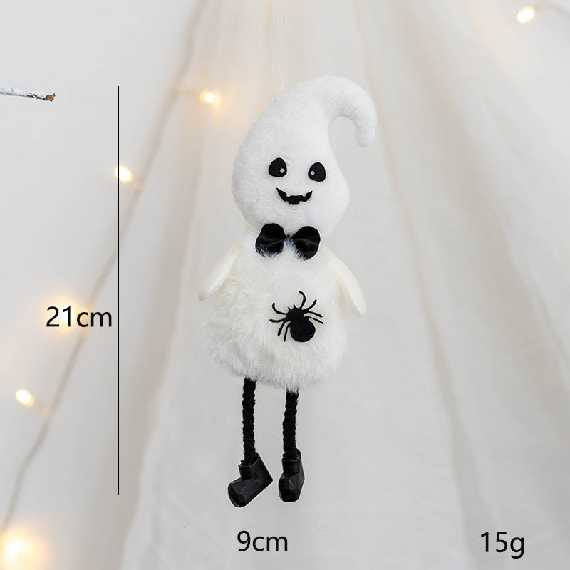 Plush ghost hanging decoration with a smile, black eyes, and a bow tie. It has a spider design on its belly, black rope legs, and is 21cm tall and 9cm wide.