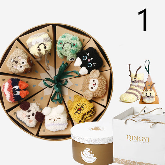 Box of colorful, animal-themed socks arranged in a circle, each in individual cone-shaped packaging. Includes a round gift box and a white shopping bag with "QINGYI" printed on it.
